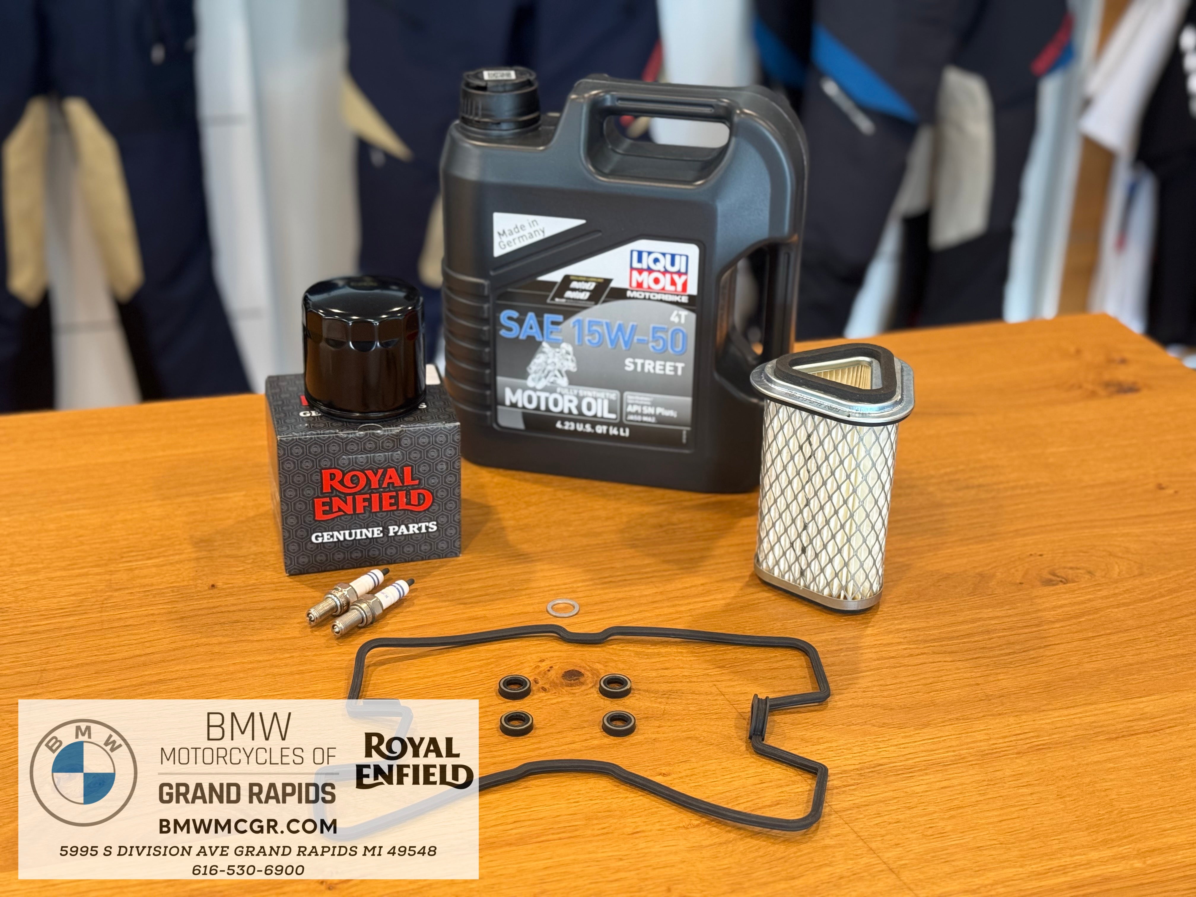 Motorcycle oil, filter, and other parts on a wooden table with BMW and Royal Enfield branding.